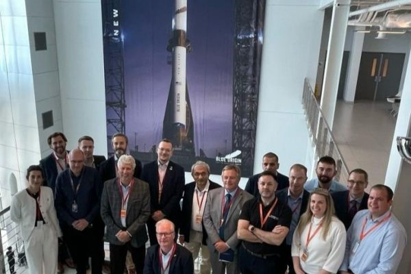 Group photo of 17 people in front of a large image of a rocket. Image Source: Business Durham.
